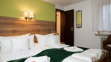 A hotel room with a wooden headboard, two bedside lamps, a green throw blanket, and neatly folded towels on the bed.