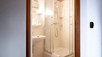 A glass-enclosed shower stall with a white sink and a towel hanging on the door.