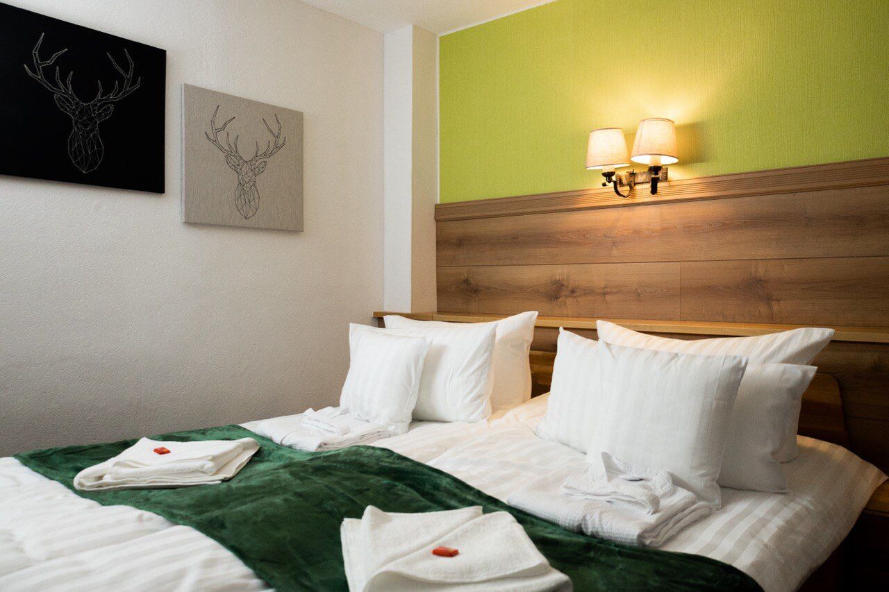 A hotel room with a wooden headboard, two wall-mounted lamps, a green accent wall, and artwork of deer heads.