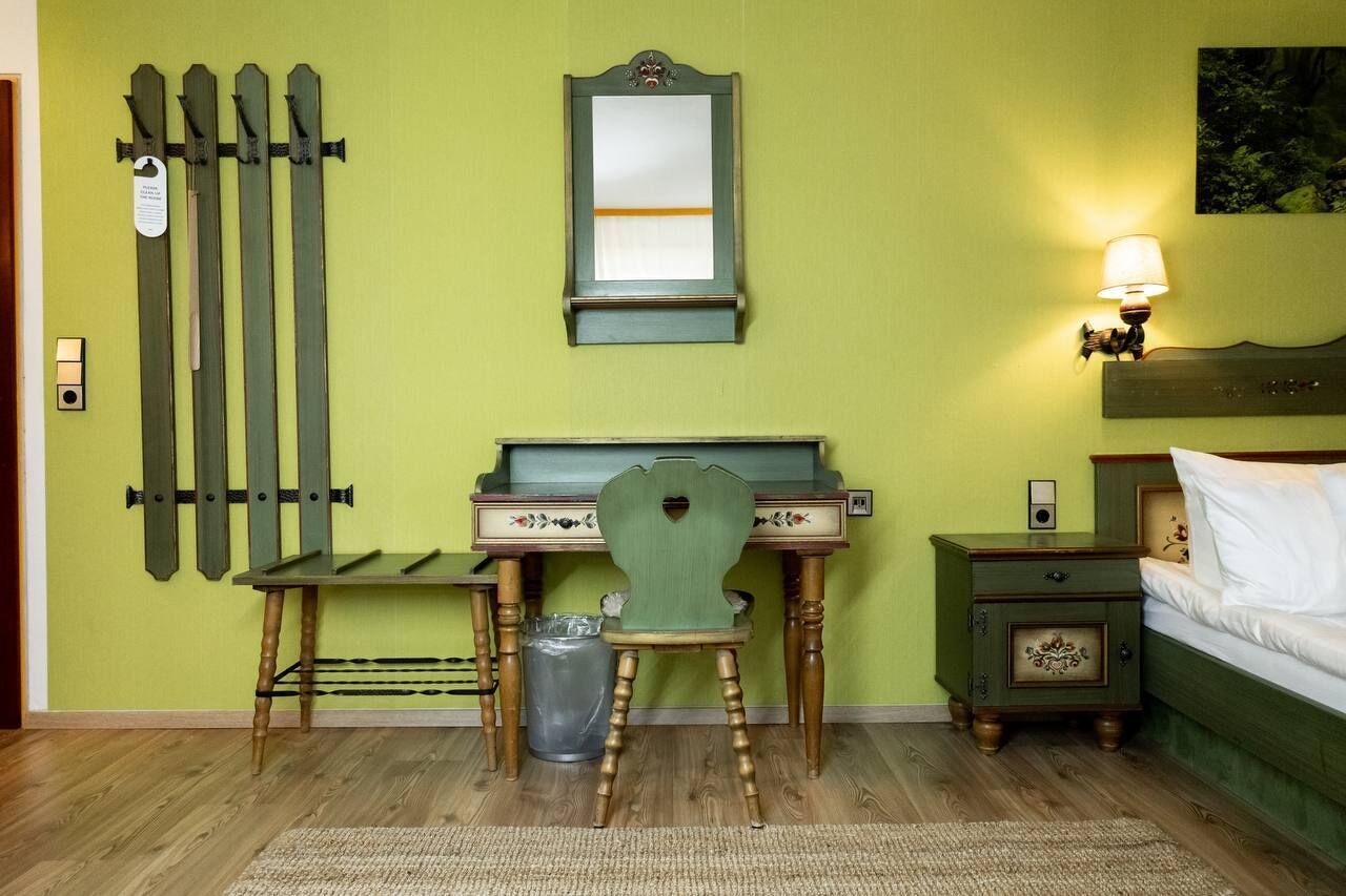 Een kamer met een bureau, stoel, bed, nachtkastje en een spiegel aan de muur.