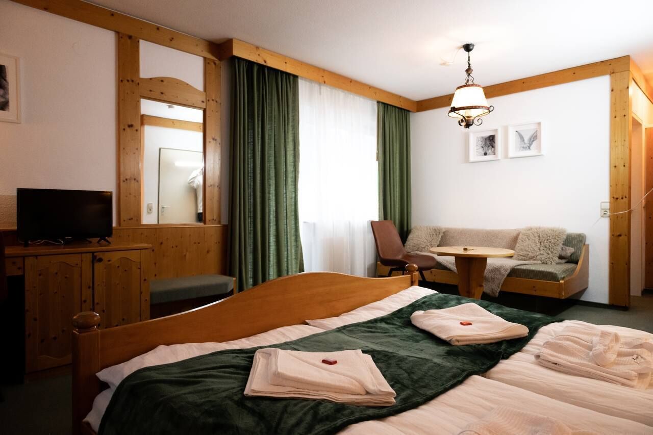 A hotel room with a wooden bed, a desk with a television, a sofa, and a small table.