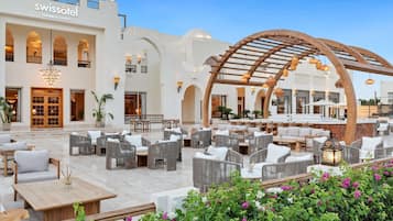 A hotel lobby with outdoor seating, a bar area, and a large arched wooden structure.