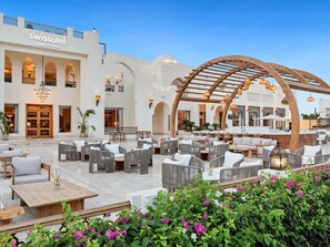 A hotel lobby with outdoor seating, a bar area, and a large arched wooden structure. - Swissôtel Sharm El Sheikh All Inclusive Collection (Sharm El Sheikh)