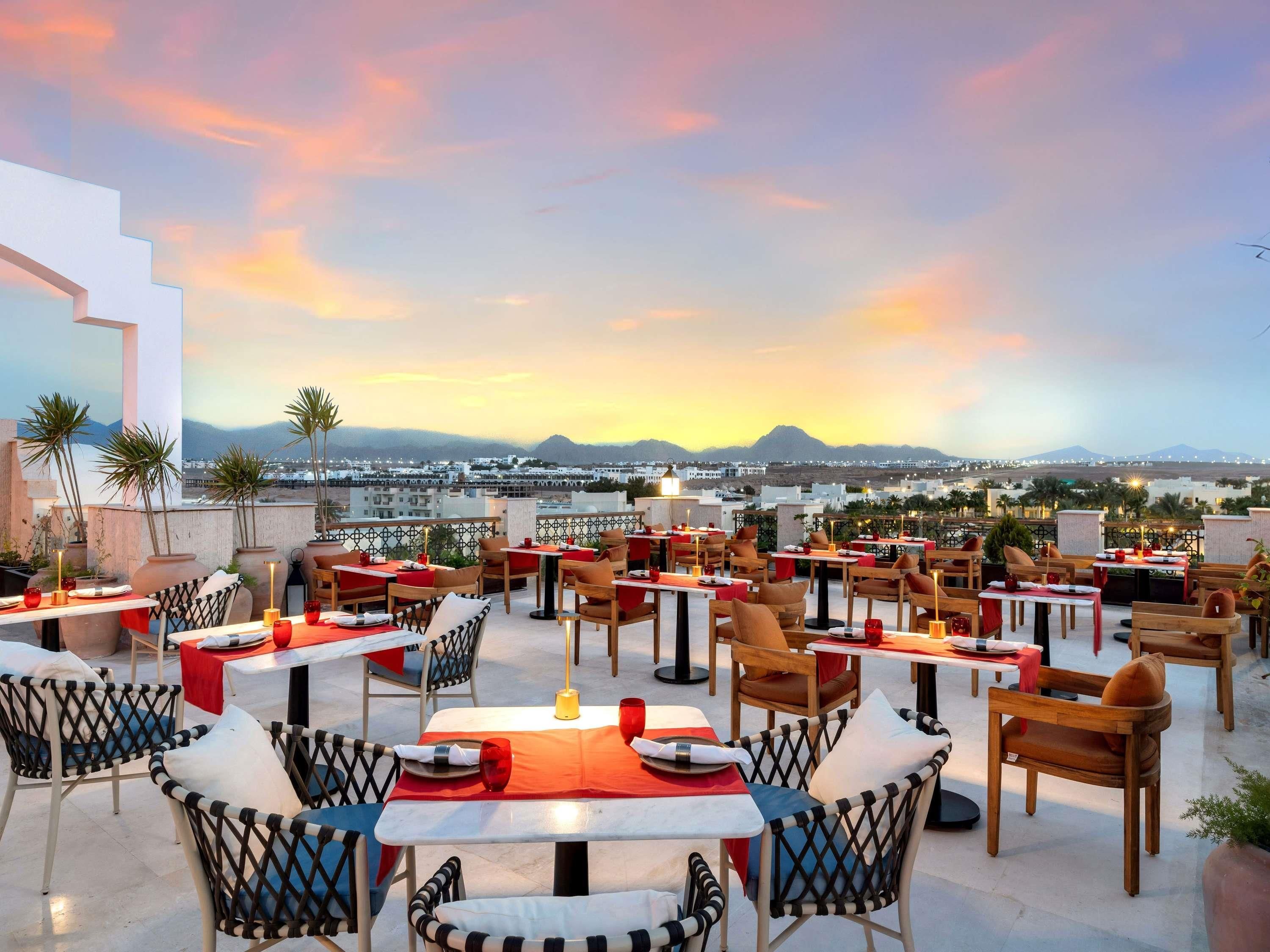 An outdoor dining area with tables and chairs, a view of a cityscape, and mountains in the distance.