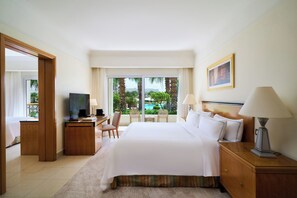A hotel room with a large bed, a desk with a television, a chair, and a view of palm trees and a pool. - Swissôtel Sharm El Sheikh All Inclusive Collection (Sharm El Sheikh)