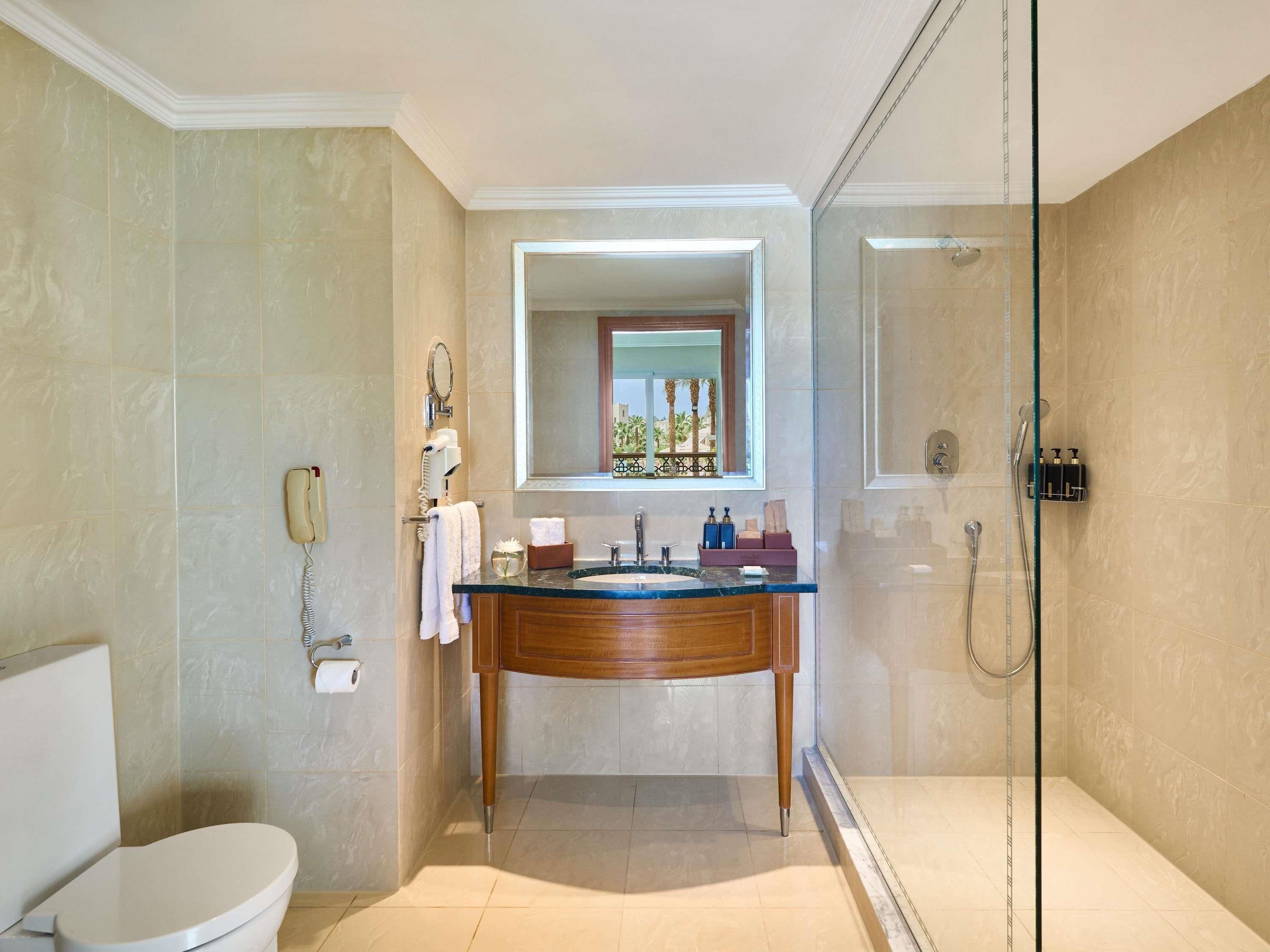 Une salle de bain comprenant des toilettes, un lavabo avec un miroir, une douche et un espace de douche délimité par des parois en verre.