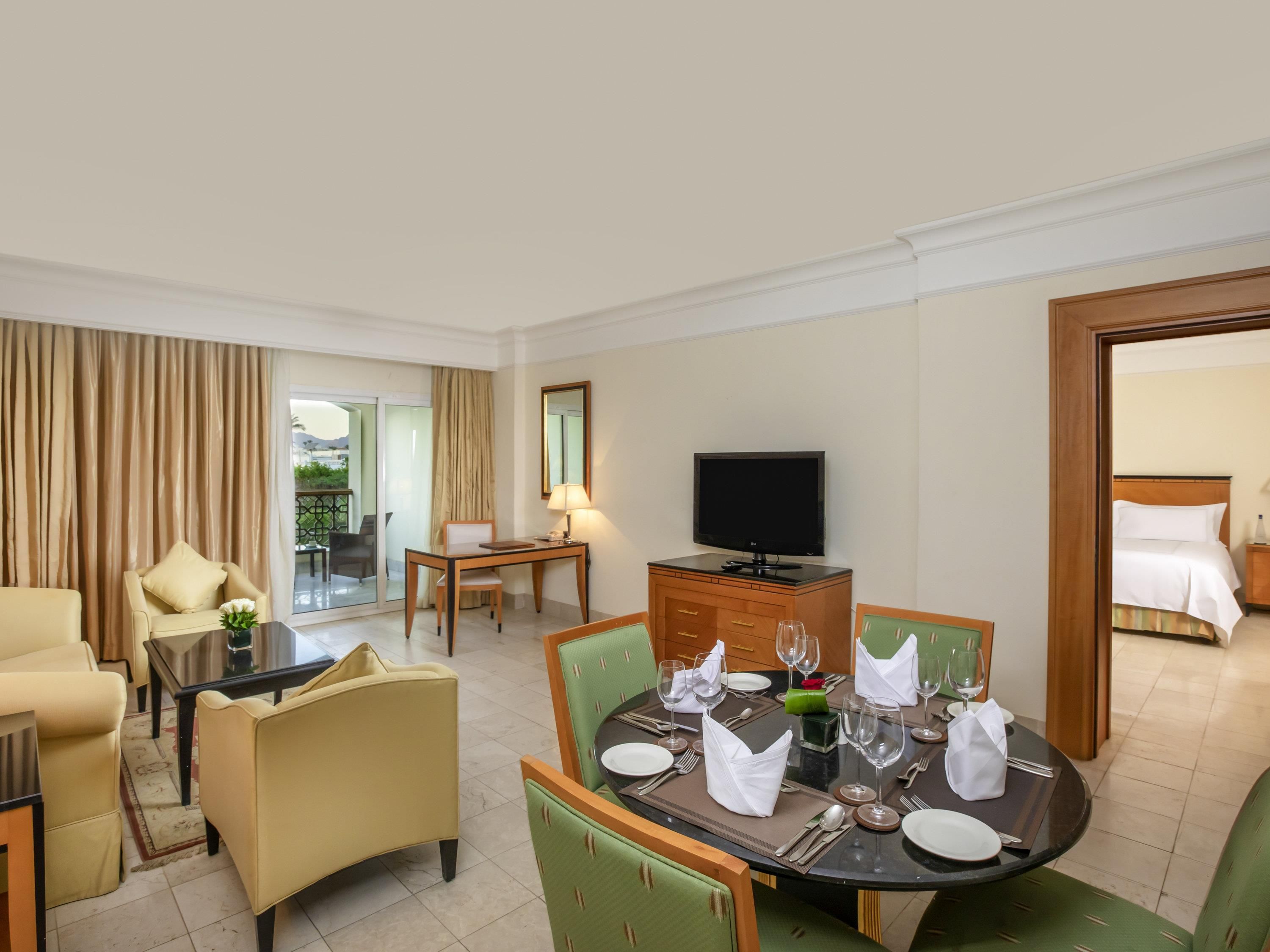 A hotel room with a dining area, a TV, and a bed.