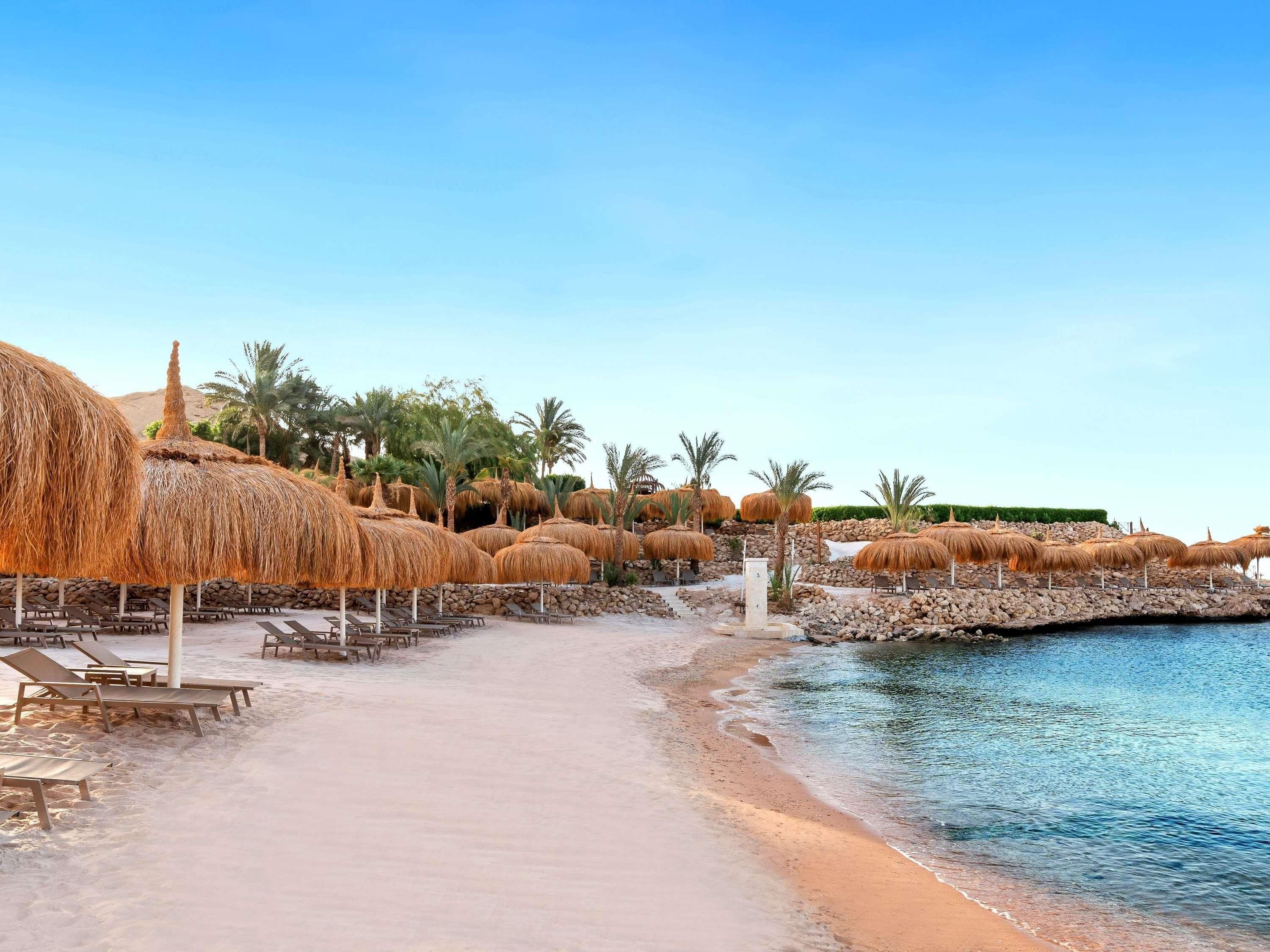 A beachside resort with thatched umbrellas, lounge chairs, and a rocky shoreline.