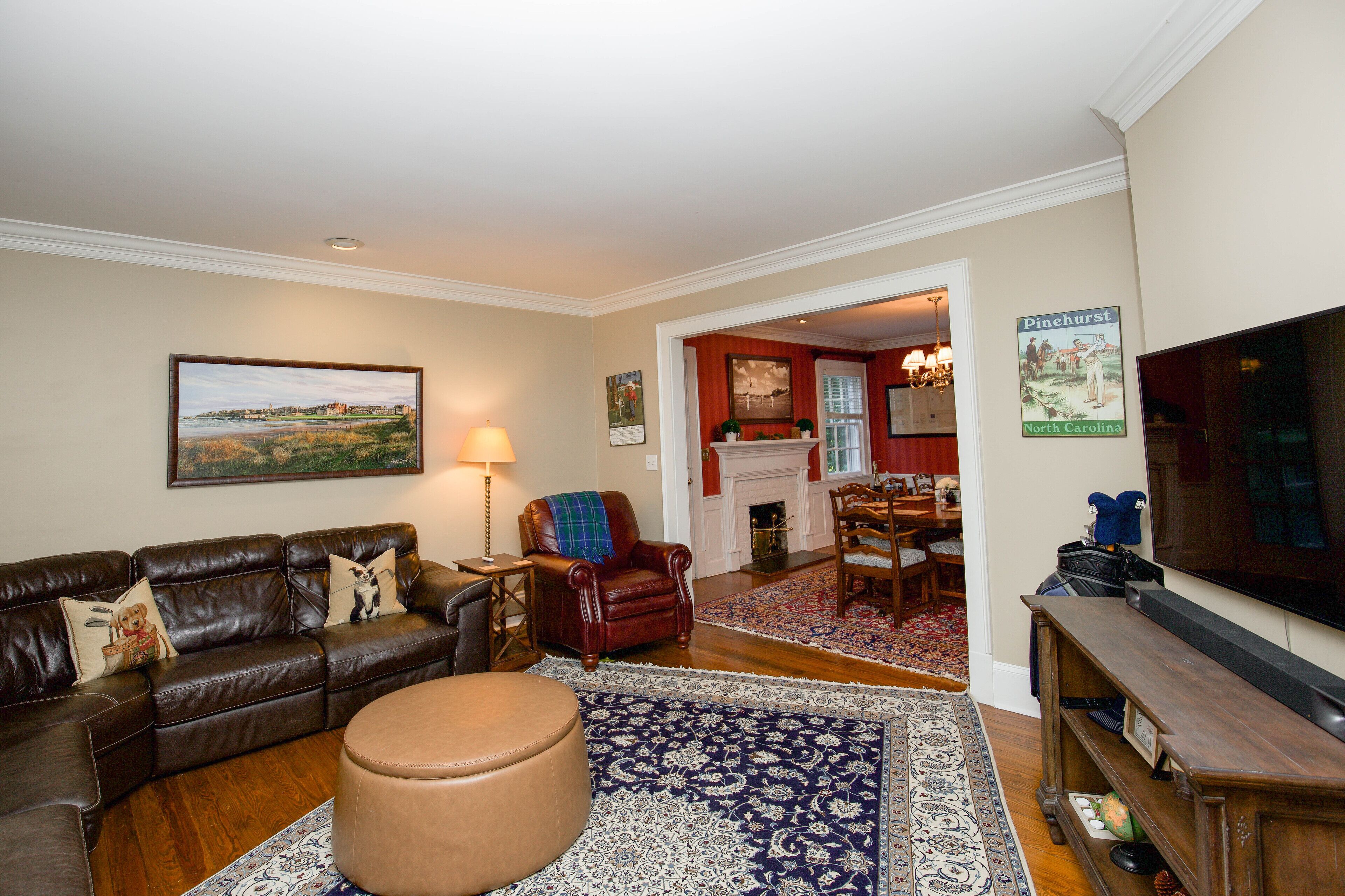 A living room with a leather couch, a round ottoman, a television, and a fireplace in the background.