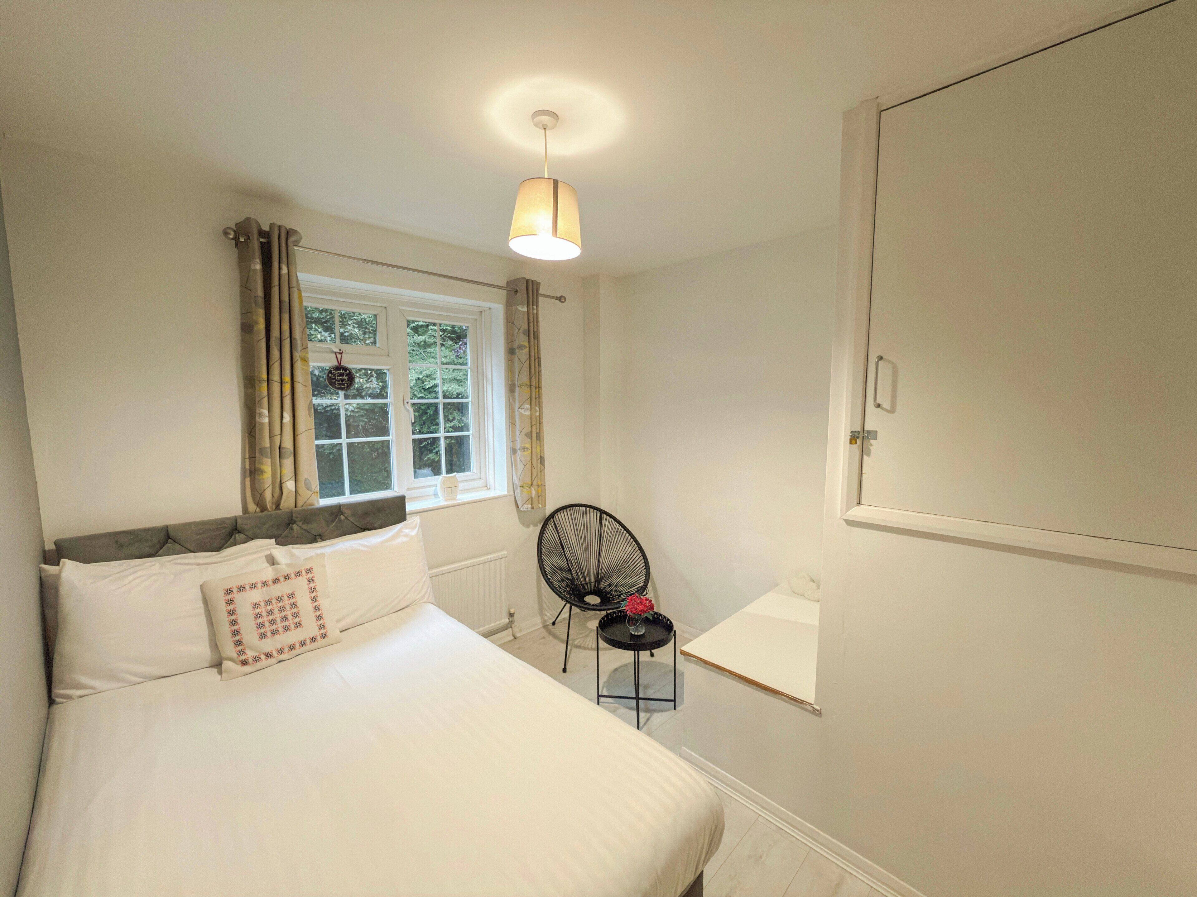 Un dormitorio con cama, ventana, silla y mesita de noche.
