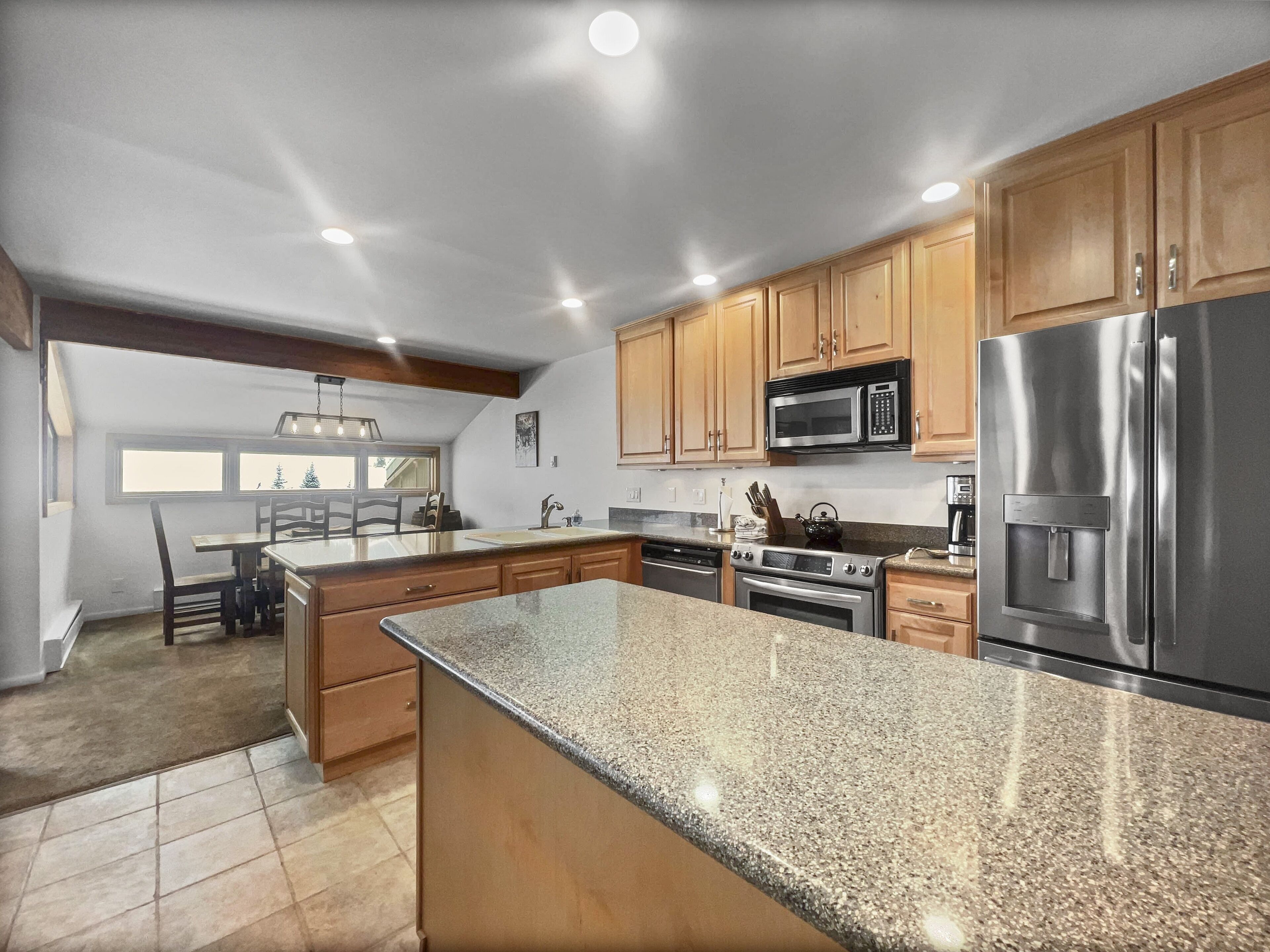 A kitchen with granite countertops, wooden cabinets, stainless steel appliances, and a dining area with a view.