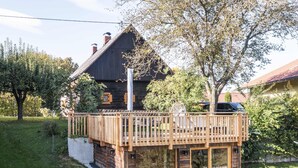 Eine Holzhütte mit einer Terrasse, umgeben von viel Grün und Bäumen.