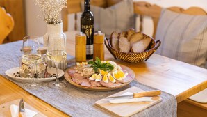 Ein Esstisch mit einem Teller mit Schinken, gekochten Eiern und einem Glas Weißwein, dazu eine Weinflasche, eine Blumenvase und ein Brotkorb.