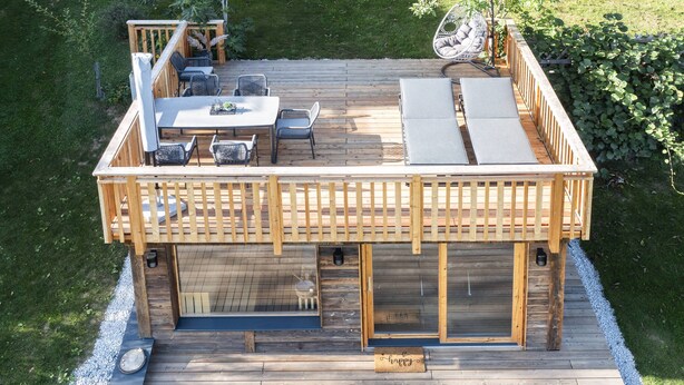 Eine Holzterrasse mit Essbereich, Sitzgelegenheiten und einem kleinen Garten.