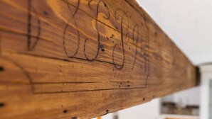 Ein Holzbalken mit rustikalem Design, eine moderne Küche mit weißen Schränken und einem eingebauten Ofen sowie ein helles Fenster mit gelbem Rahmen.