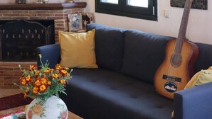Een woonkamer met een bank, een gitaar, een vaas met bloemen en een open haard.