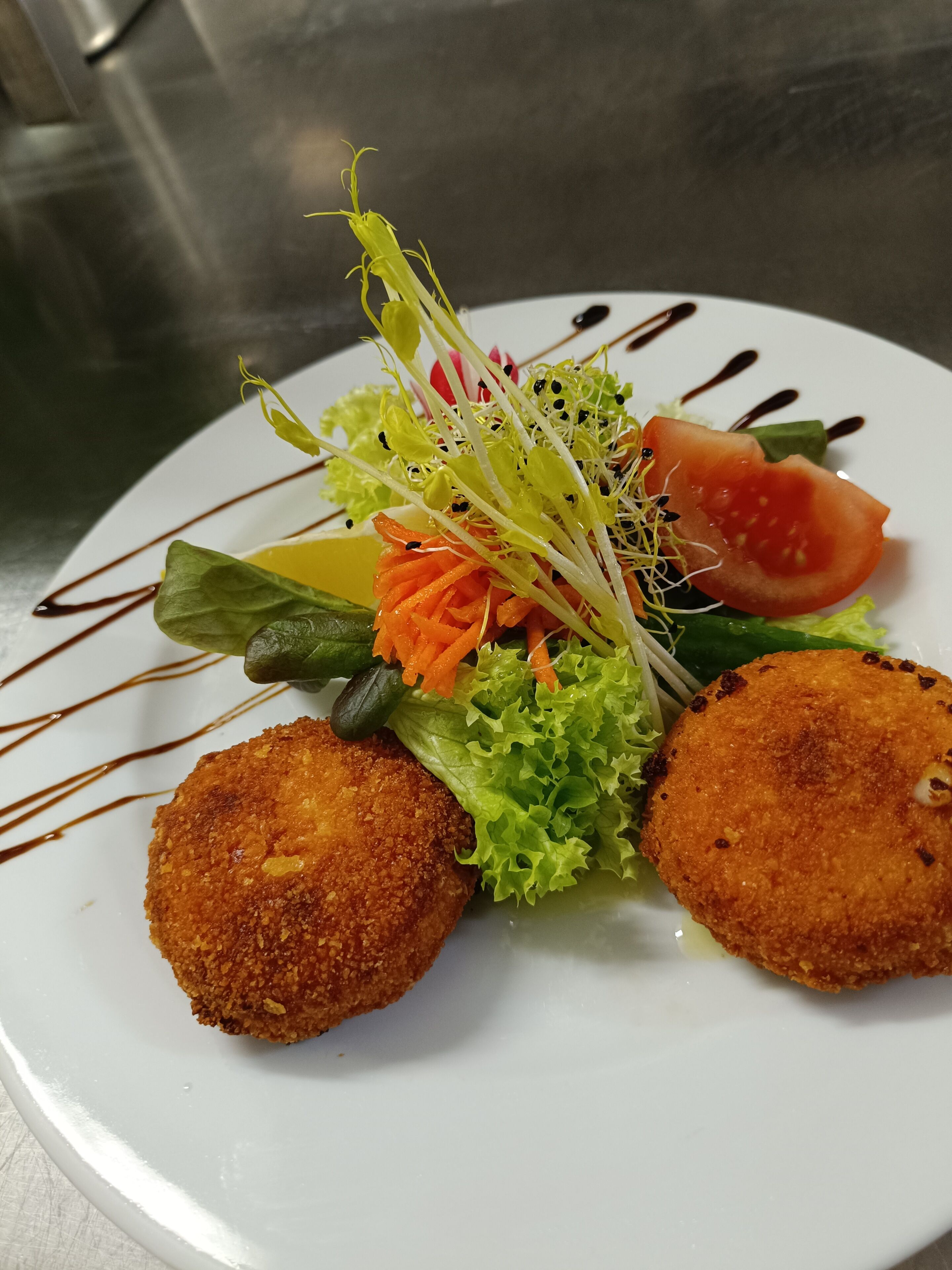 A plate with two breaded items, a salad with lettuce, carrot, and tomato, and a decorative drizzle.