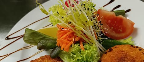A plate with two breaded items, a salad with lettuce, carrot, and tomato, and a decorative drizzle.