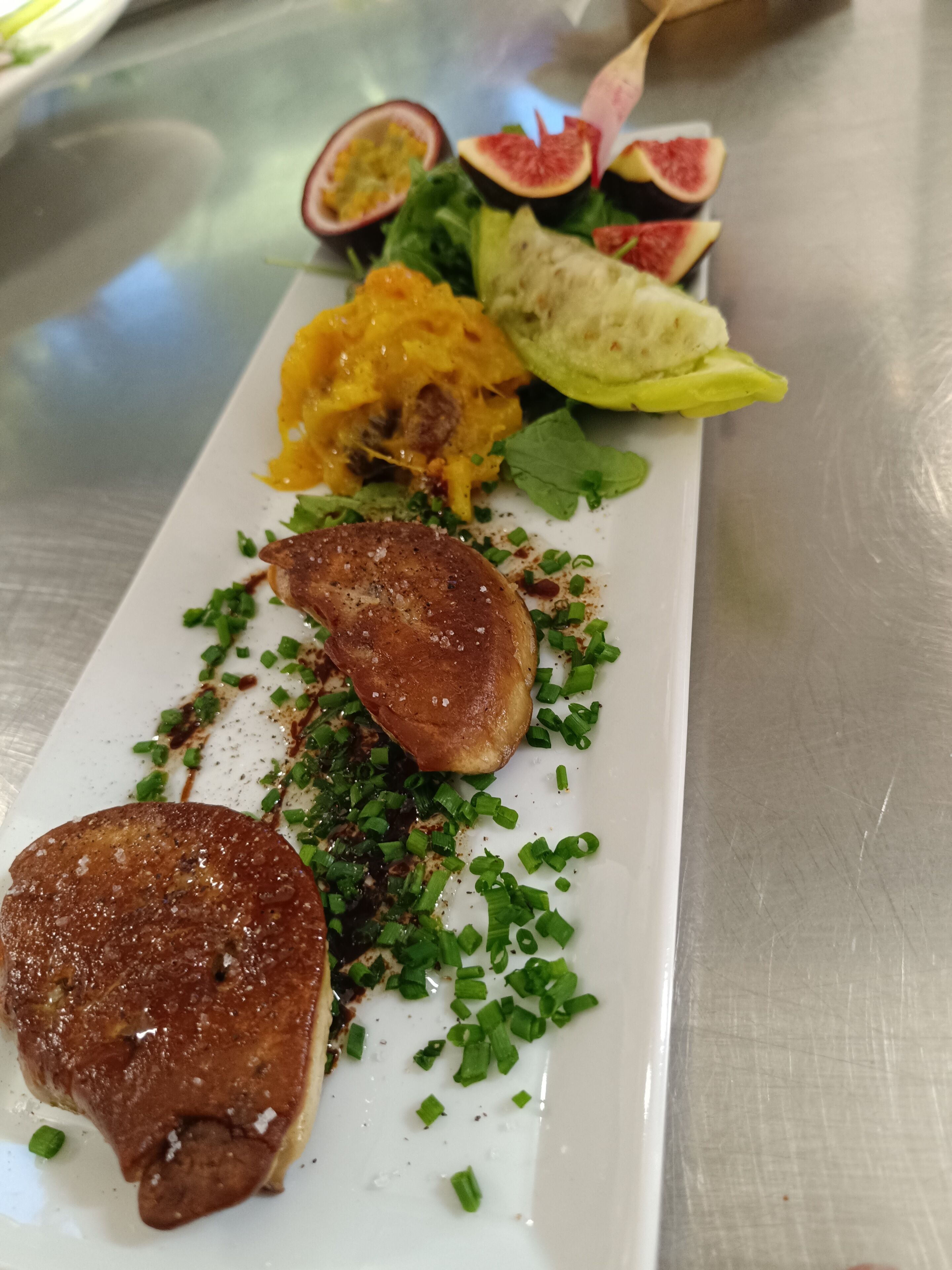 A plated dish with various food items including a piece of meat, greens, and a yellow sauce.