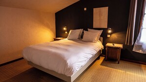 Una cama bien hecha con ropa blanca en una habitación con paredes oscuras, dos mesitas de noche y una lámpara en cada pared.