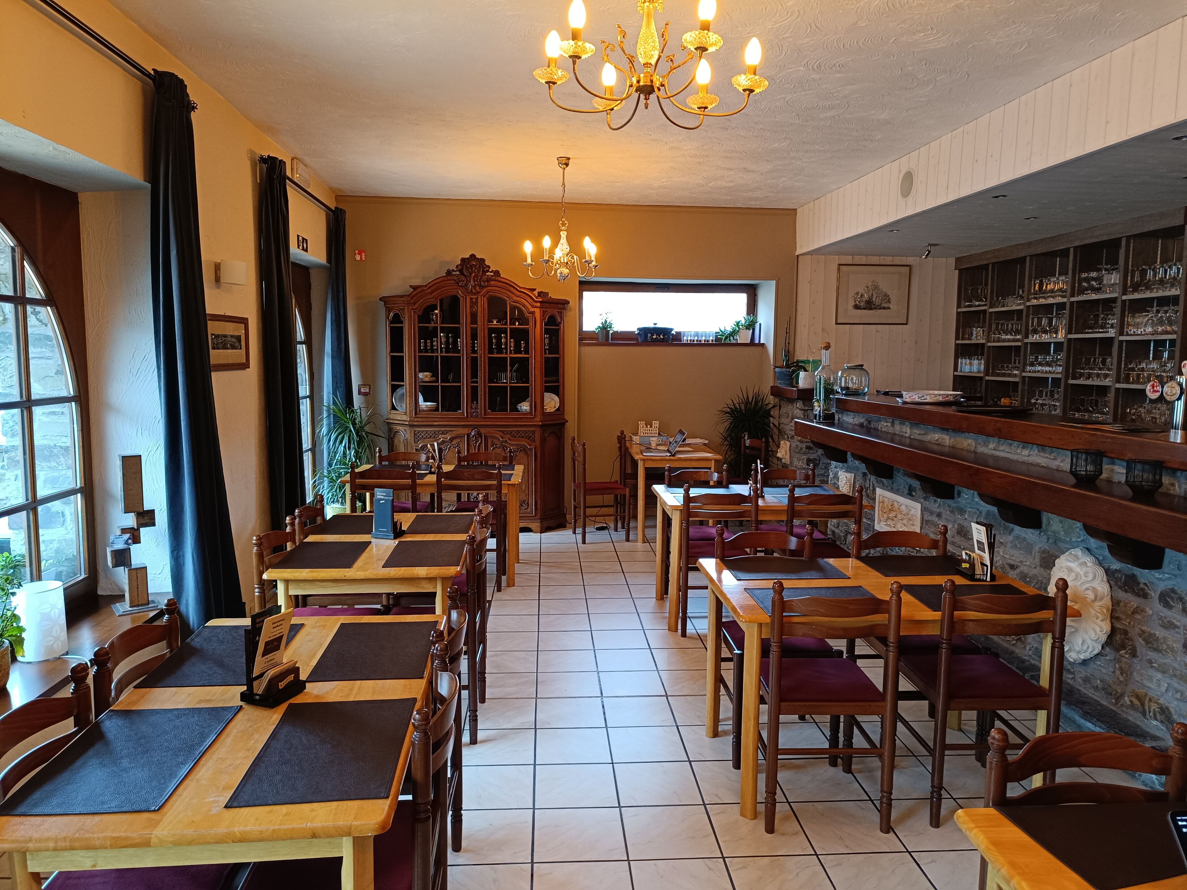 Un restaurante con mesas y sillas de madera, una zona de bar y un amplio armario de madera con puertas de cristal.
