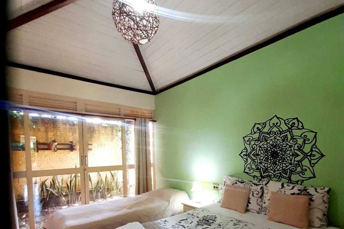 A room with two beds, a large window, and a green wall with a mandala design.