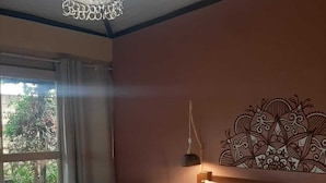 A bedroom with two beds, a decorative headboard, a bedside lamp, and a view of greenery outside. - Pousada Paralelo 14 (Alto Paraíso de Goiás)