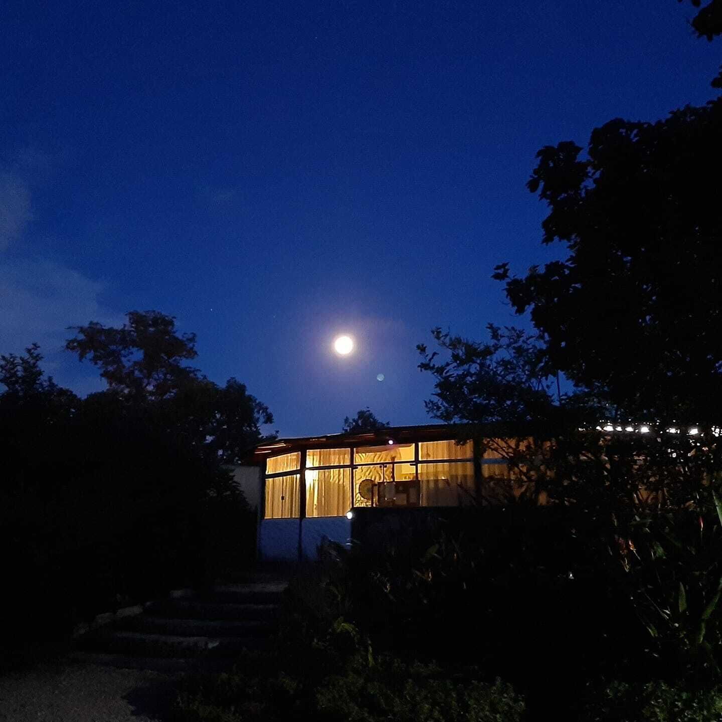 Un bâtiment doté de grandes fenêtres, avec la lune visible dans le ciel.