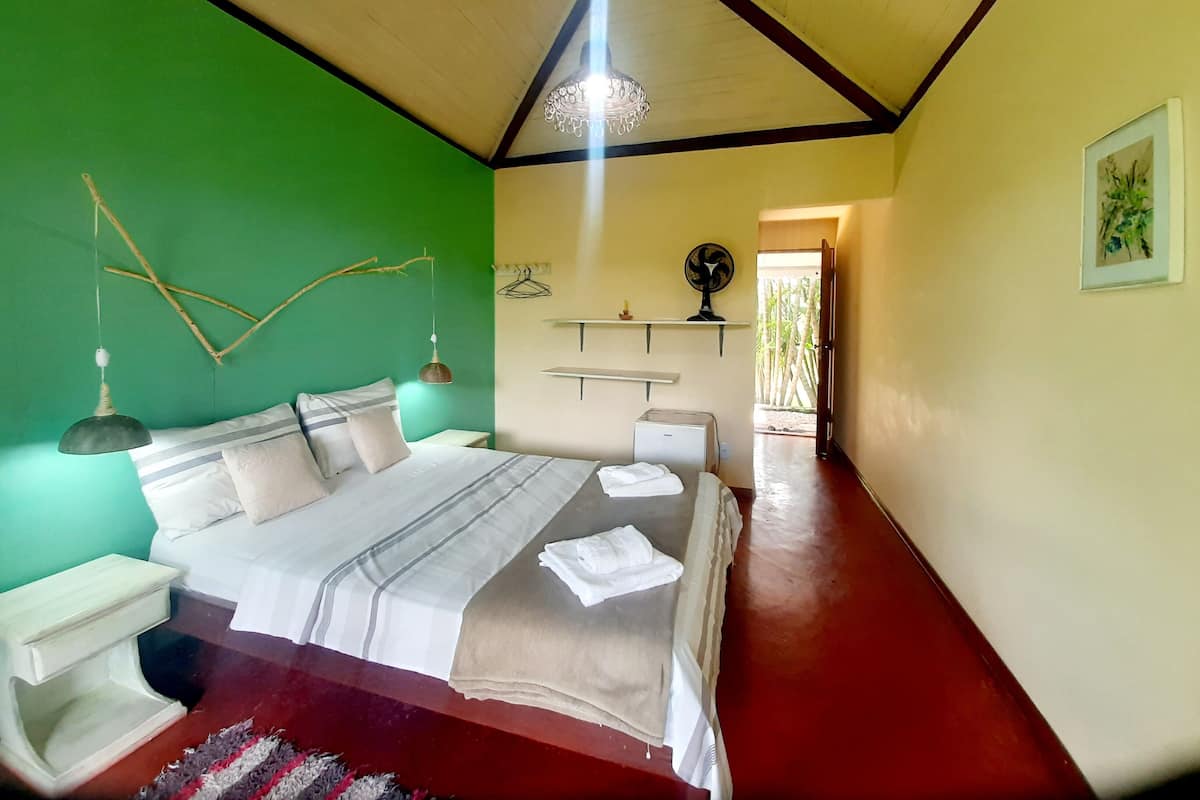 A bedroom with a bed, bedside tables, a hanging lamp, a fan, and a shelf with a picture.