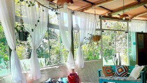 A cozy, rustic room with a wooden ceiling, a stone bench with cushions, a small wooden table, and a view of greenery outside. - Pousada Paralelo 14 (Alto Paraíso de Goiás)