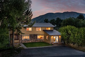 Eine zweistöckige Holzhütte mit Steinfundament, großen Fenstern und einer kleinen angebauten Garage.