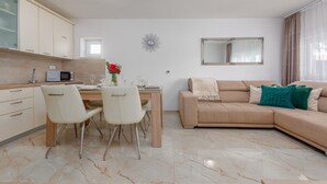 Una cocina moderna con armarios blancos, una zona de comedor con mesa y sillas, un sofá color beige y un espejo grande.