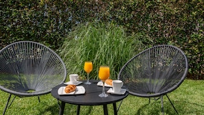 Una mesa con dos sillas, un croissant, dos tazas y dos vasos de jugo de naranja.