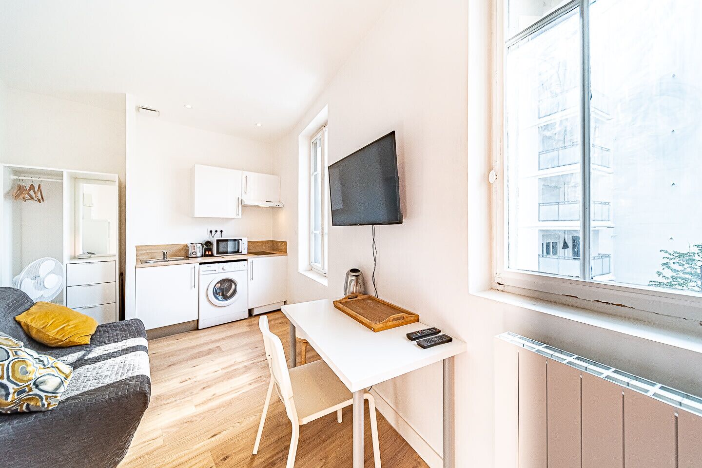 Een ruimtelijke leefruimte met kitchenette, eethoek en groot raam met uitzicht op de buitenkant van het gebouw.