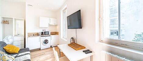 Een ruimtelijke leefruimte met kitchenette, eethoek en groot raam met uitzicht op de buitenkant van het gebouw.