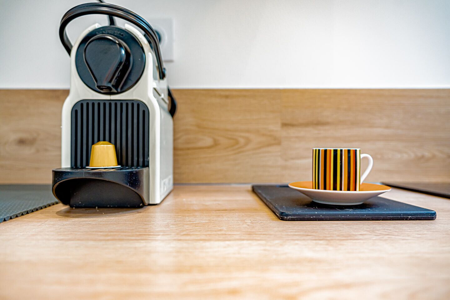 A modern kitchen with a kettle and a striped mug on a coaster.