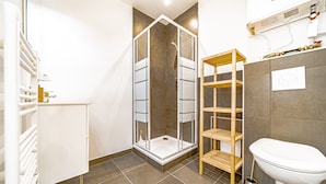 Une salle de bain moderne avec une douche à parois de verre, des toilettes et une étagère en bois.