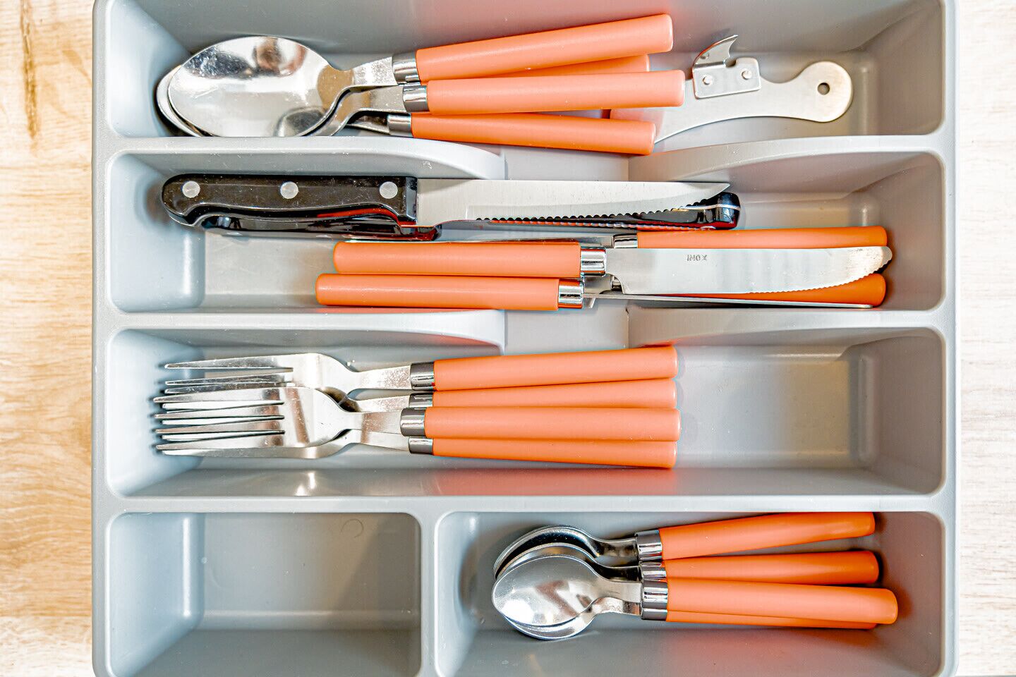 Un porte-ustensiles avec des manches orange, contenant divers outils de cuisine, comme une cuillère, un couteau et une fourchette.