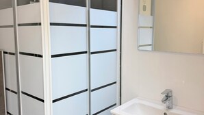 Une salle de bain avec un lavabo blanc, un miroir et une cloison en verre dépoli.