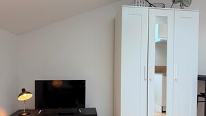 Une pièce avec un téléviseur posé sur un meuble noir, une armoire blanche et une petite statue sur le meuble.