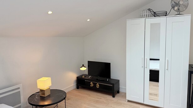 Une chambre avec un puits de lumière, un lit, une télévision, une armoire et une petite table avec une lampe.