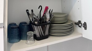 Et køkkenskab med to hylder, hvor den ene indeholder stablede tallerkener og den anden en bestikholder med knive og gafler.