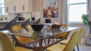 Uma cozinha moderna com uma mesa de jantar de vidro, cadeiras amarelas, armários brancos e uma janela grande.
