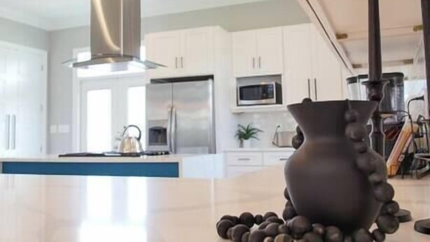 Uma cozinha moderna com armários brancos, eletrodomésticos de aço inoxidável e uma ilha central com um vaso decorativo.