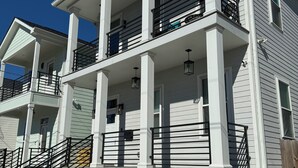 Um edifício residencial de dois andares com uma varanda no segundo pavimento, um alpendre frontal coberto e fundação de tijolos.