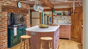 Una cocina con una isla central, taburetes de madera, pared de ladrillo y una campana colgante.