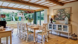 Un comedor con una mesa y sillas de madera, un mueble con puertas de cristal y vistas a un jardín con juegos.