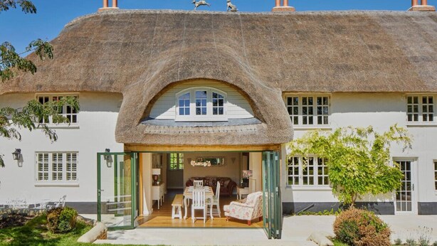 Una casa con techo de paja, un arco central, un comedor y un jardín.