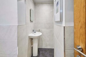 A narrow bathroom with a white pedestal sink, tiled walls, and a wooden door. - Host & Stay | Millers Coach House (Hexham)