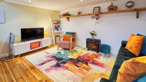 A modern living room with a flat-screen TV, a wooden floor, a colorful rug, a green sofa, and a bookshelf. - Host & Stay | Millers Coach House (Hexham)